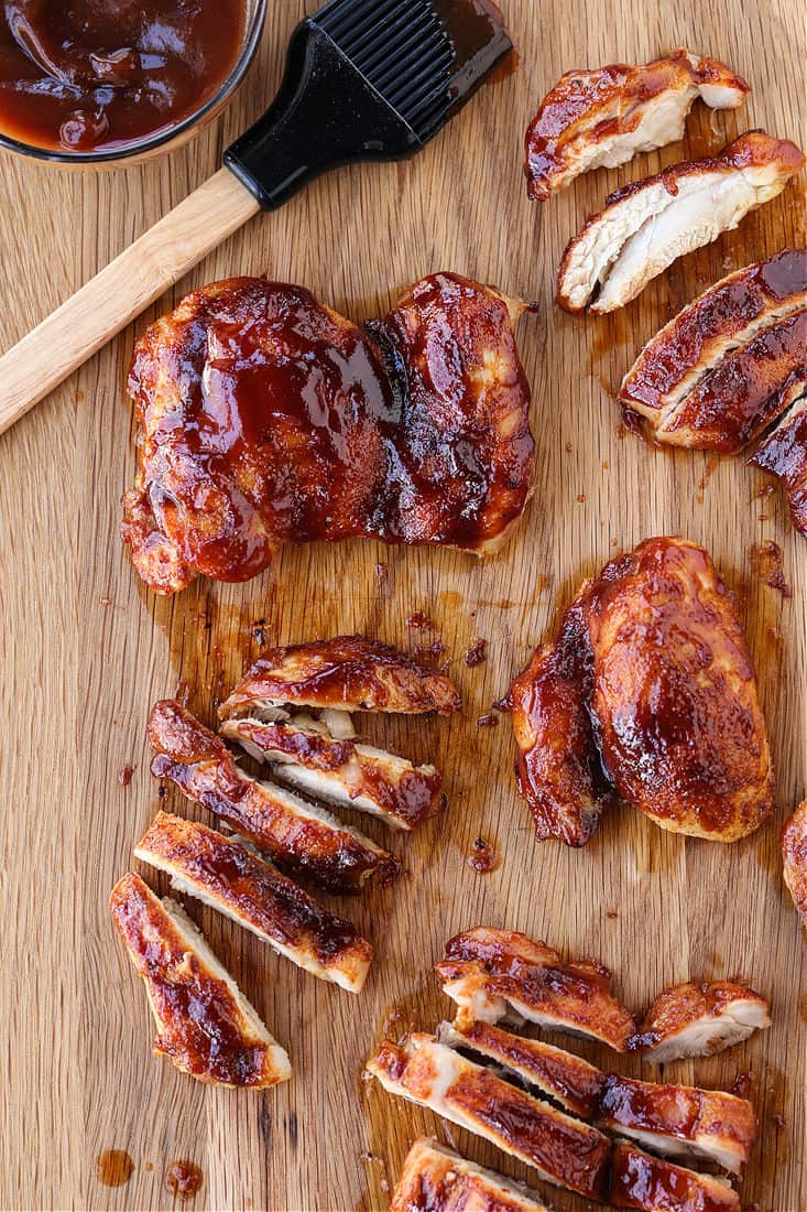 BBQ boneless chicken thighs on a cutting board with sauce