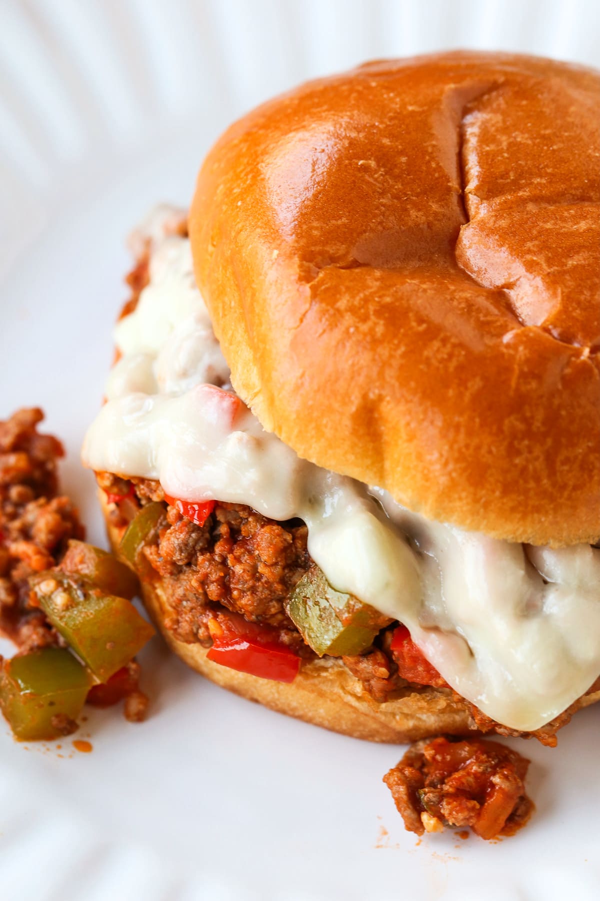Italian Sloppy Joes are an easy dinner recipe that everyone loves! An Italian twist to a sloppy joe with peppers, onions and melted cheese! sloppy joe sandwich from the top on white plate