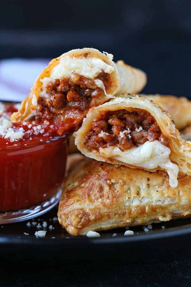 Puff Pastry Pizza Pockets cut in half on a plate with sauce