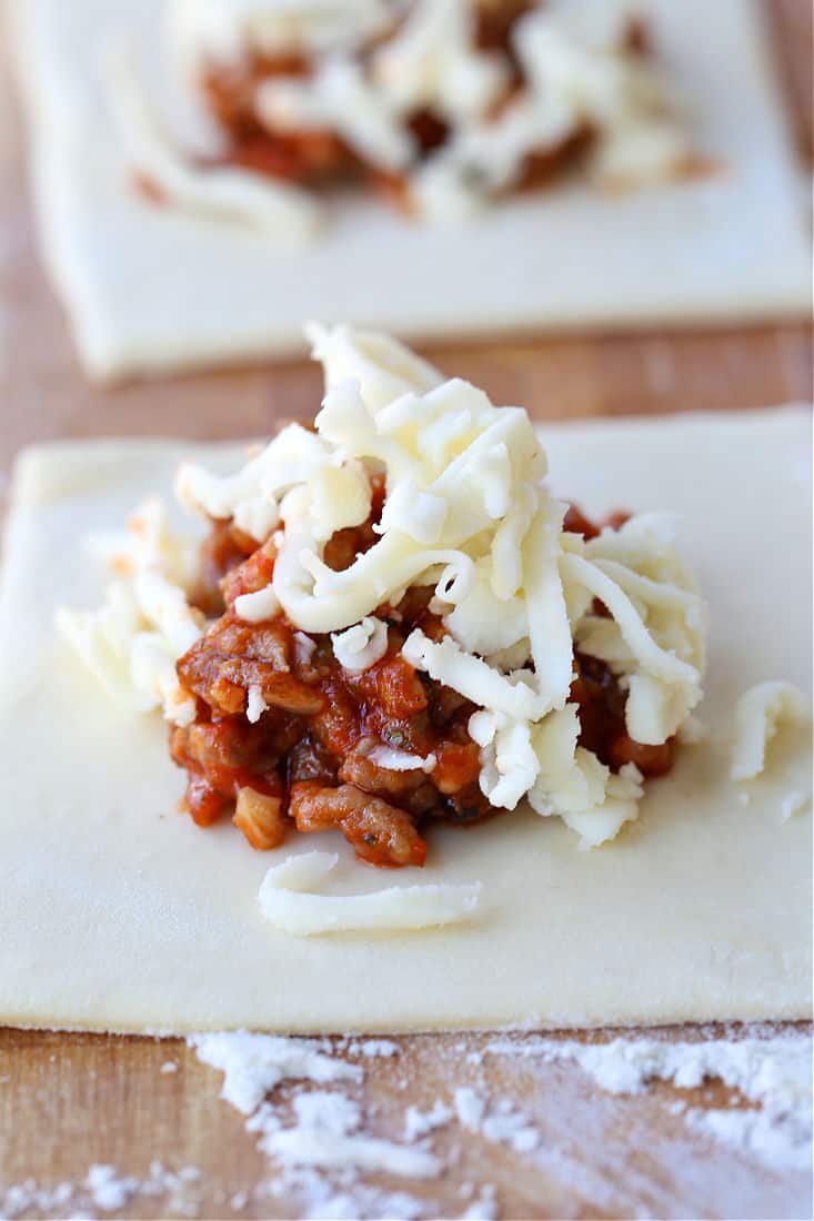 Puff Pastry Pizza Pockets are a family favorite recipe! Puff pastry filled with sausage, mushrooms and cheese make addicting appetizers! Mozzarella cheese and an Italian sausage filling on a puff pastry square