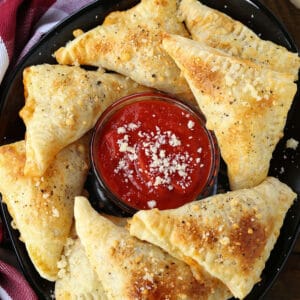 Puff Pastry Pizza Pockets on a black plate with sauce