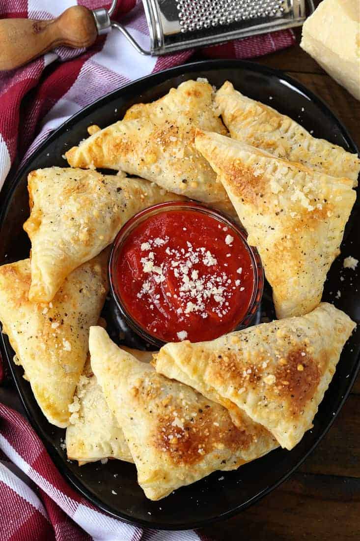 Puff Pastry Pizza Pockets on a black plate with sauce