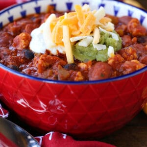 Chicken chili recipe in red bowl with cheese on top