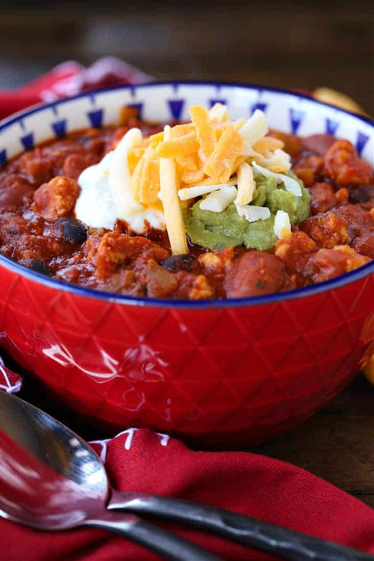 Chicken chili recipe in red bowl with cheese on top
