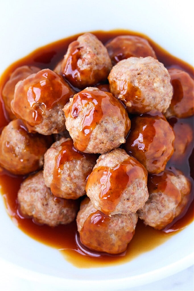 This Teriyaki Meatball recipe is one of our favorite, easy to make dinners! Oven baked, flavorful meatballs tossed in a teriyaki glaze! Meatballs in a white bowl with teriyaki glaze