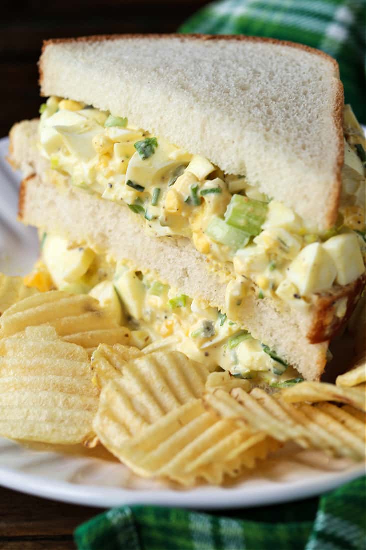 Egg salad on white bread cut in half with chips