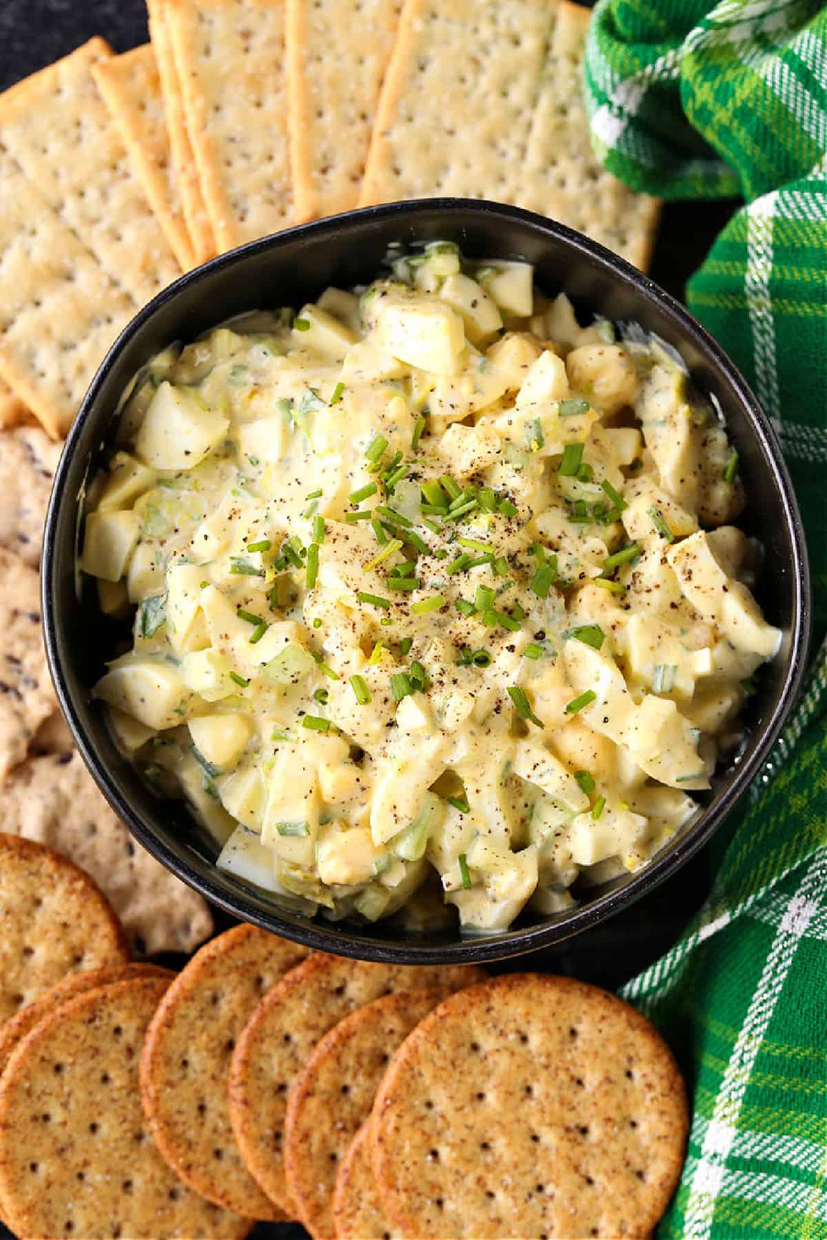 The best egg salad recipe starts with perfectly cooked hard boiled eggs! Deliciously thick, creamy and tangy with just a bit of crunch! egg salad in black bowl with crackers from top