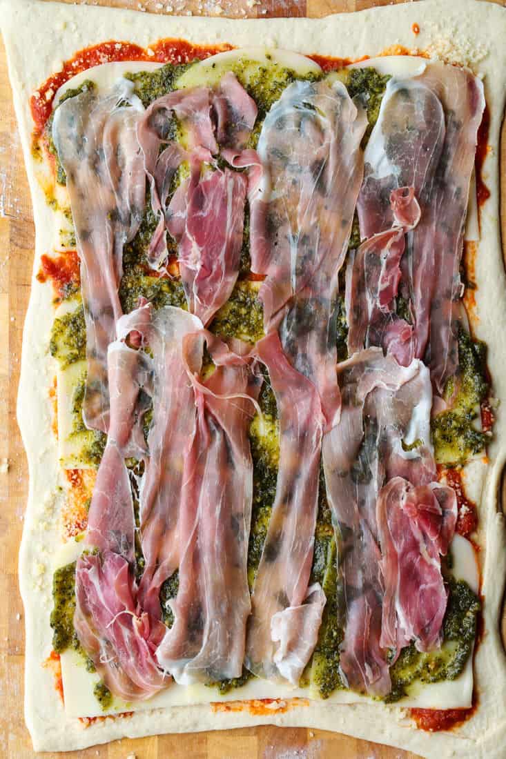 Pizza dough layered with mozzarella cheese, basil pesto and prosciutto for pizza rolls