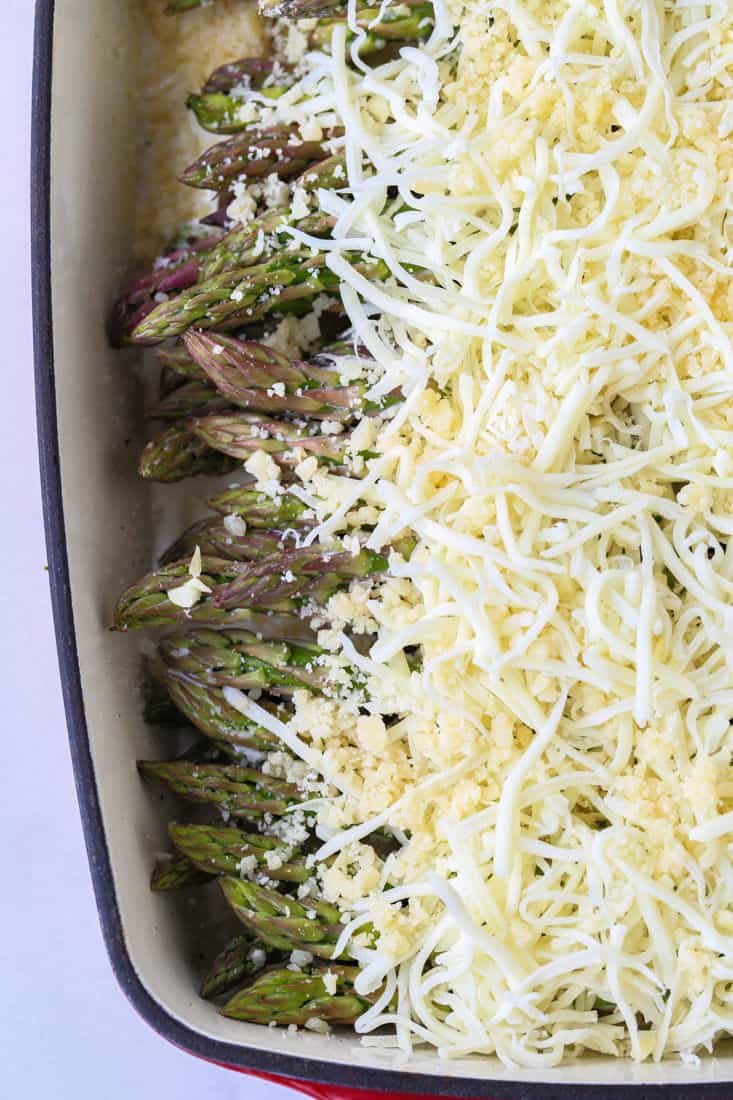Moazzarella and parmesan cheese on top of asparagus on in a baking dish