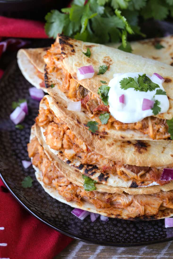 Chicken tacos on a black plate with cilantro and sour cream