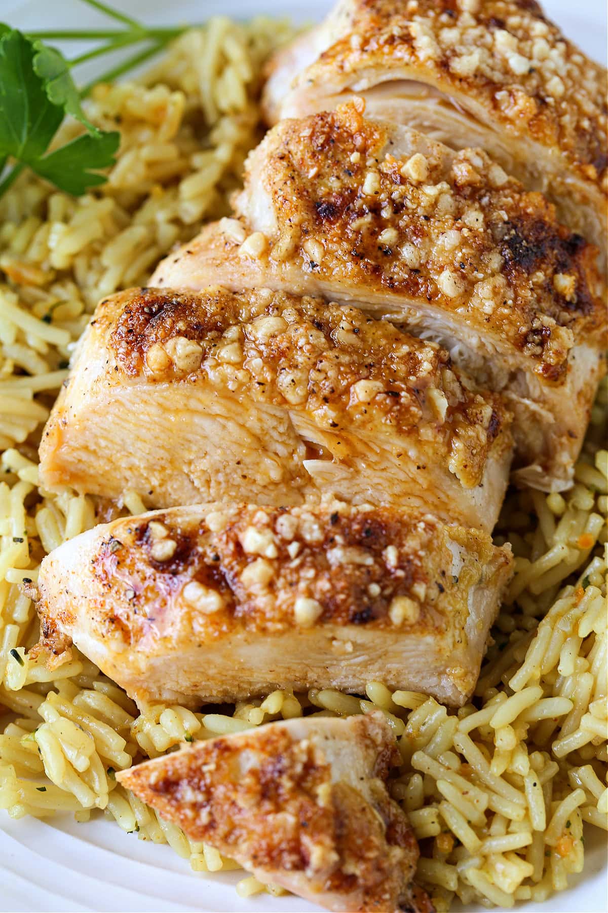 Baked Parmesan Crusted Chicken is an easy, 30 minute dinner recipe! Juicy chicken breasts baked with a tangy, parmesan crust! sliced parmesan crusted chicken breast on bed of rice pilaf
