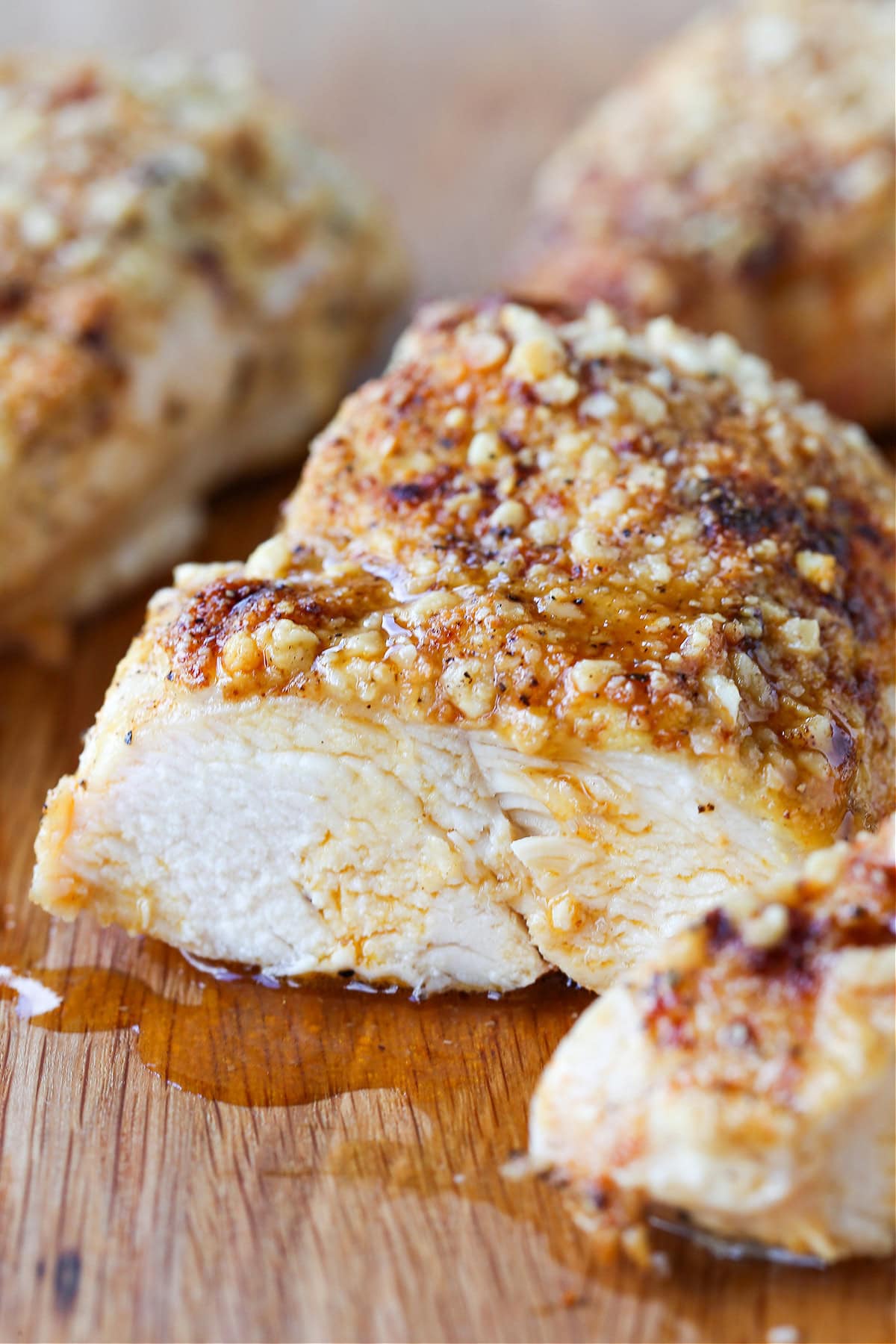 Baked Parmesan Crusted Chicken is an easy, 30 minute dinner recipe! Juicy chicken breasts baked with a tangy, parmesan crust! sliced chicken breast on wooden board with juice