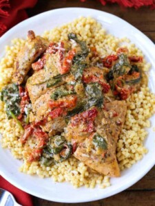 Chicken breast with sundried tomato and spinach cream sauce served over a bed of couscous on a plate.