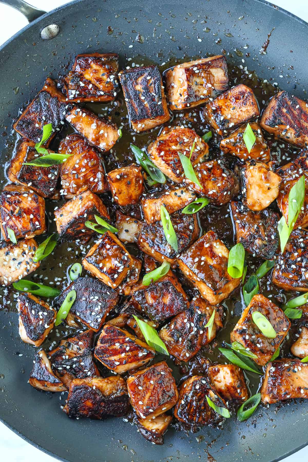 salmon bites in a skillet with scallions and sesame seeds