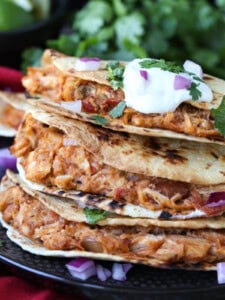 air fryer tacos with shredded chicken filling stacked on plate with sour cream