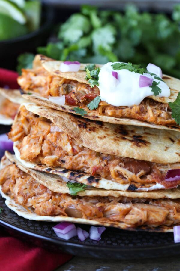 air fryer tacos with shredded chicken filling stacked on plate with sour cream