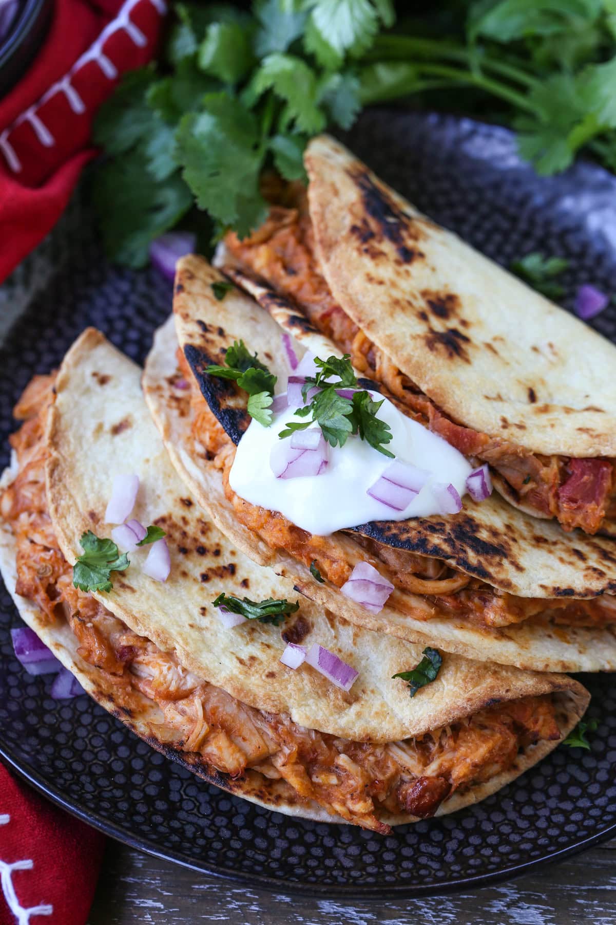 three chicken tacos on a black plate with sour cream and onions