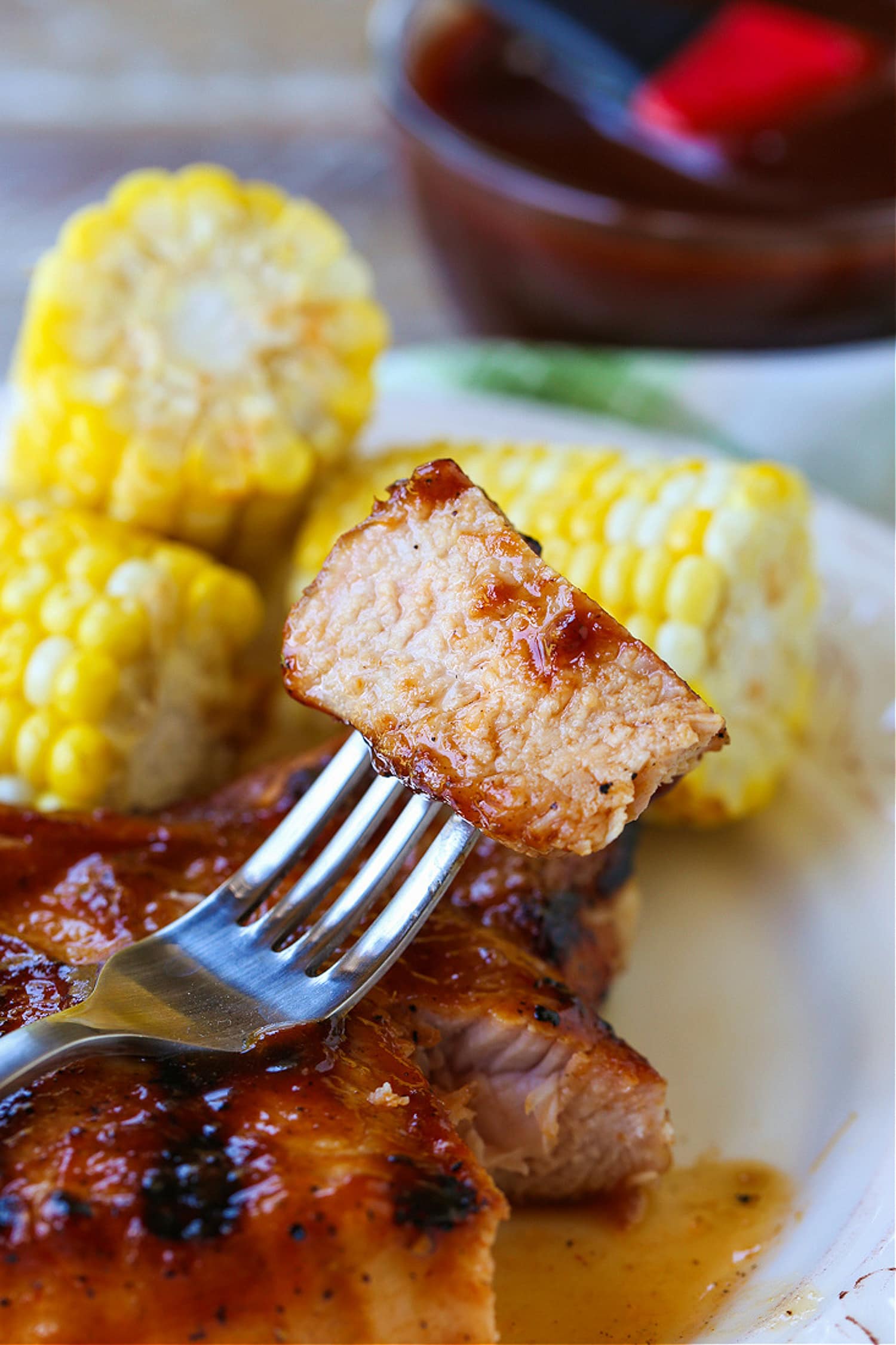 fork with a piece of bbq pork on a plate with corn