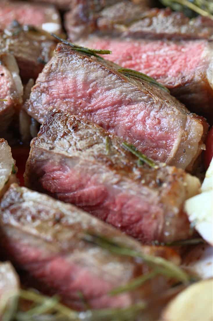 This New York Strip Steak recipe tastes as good as your favorite steak house! Tender, juicy steak made with fresh herbs, garlic and butter! sliced new york strip steak stacked on a plate