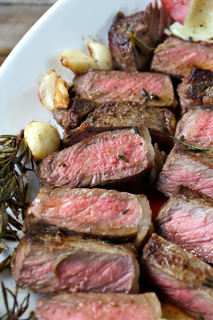 This New York Strip Steak recipe tastes as good as your favorite steak house! Tender, juicy steak made with fresh herbs, garlic and butter! new york strip steak sliced on a platter