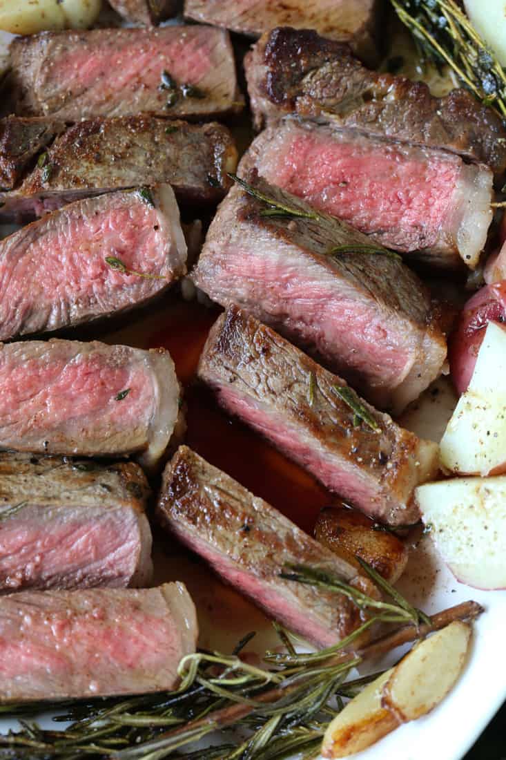 This New York Strip Steak recipe tastes as good as your favorite steak house! Tender, juicy steak made with fresh herbs, garlic and butter! sliced steak on a serving platter with potatoes