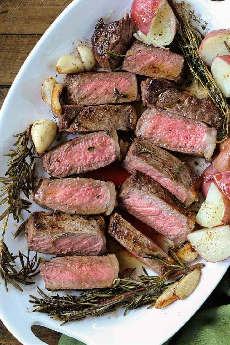 strip steak sliced on a platter with potatoes