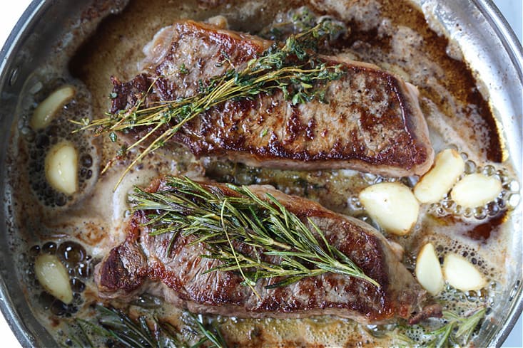 new york strip steaks seared in a skillet with herbs