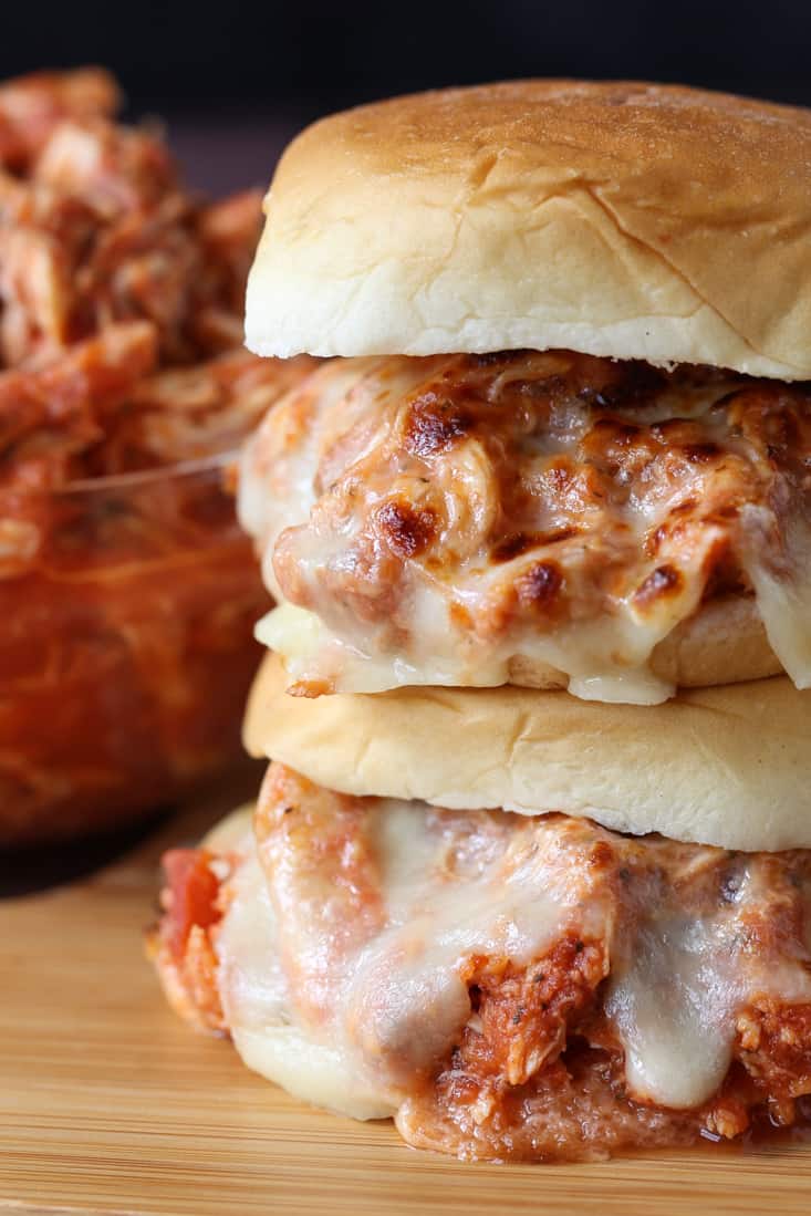 Shredded chicken sandwiches stacked on a board with cheese