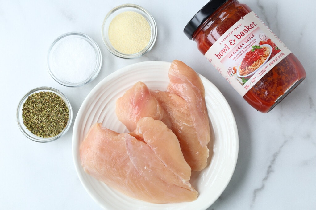 chicken breasts, seasonings and a jar of marinara sauce on marble board