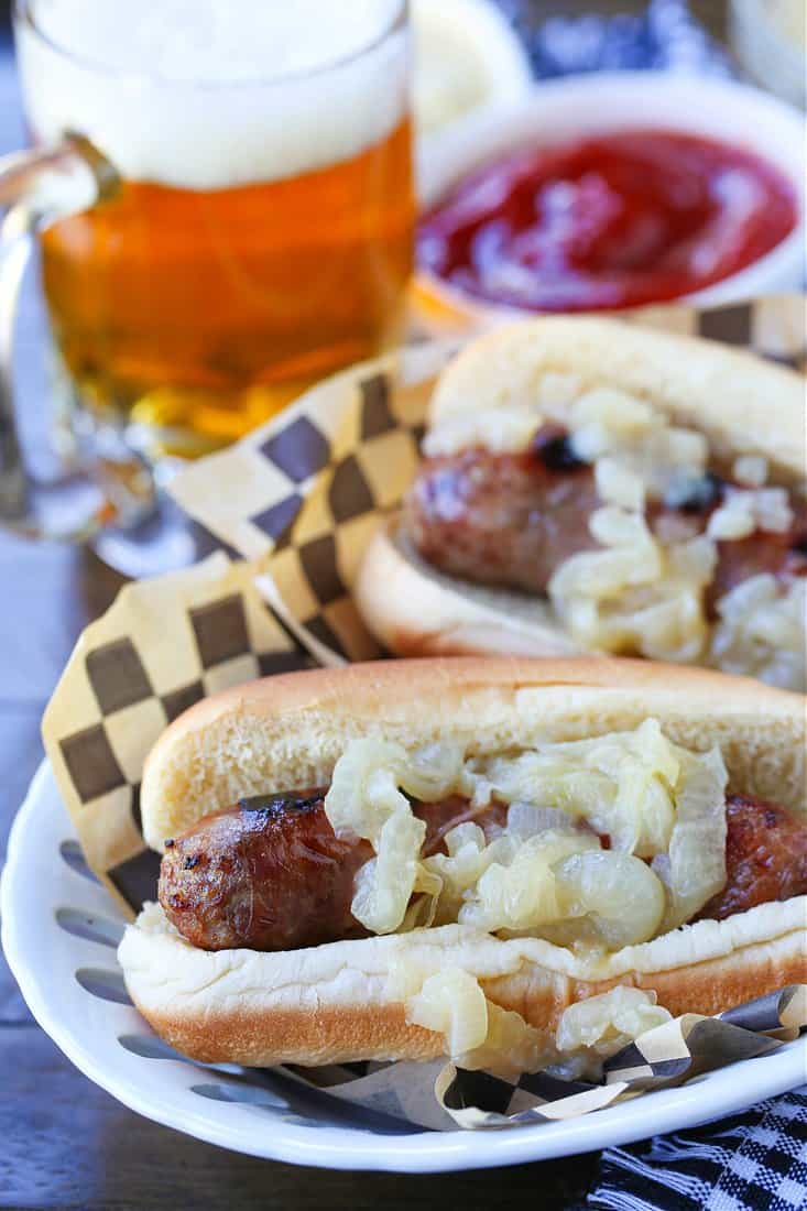 bratwurst on buns with onions and beer in background
