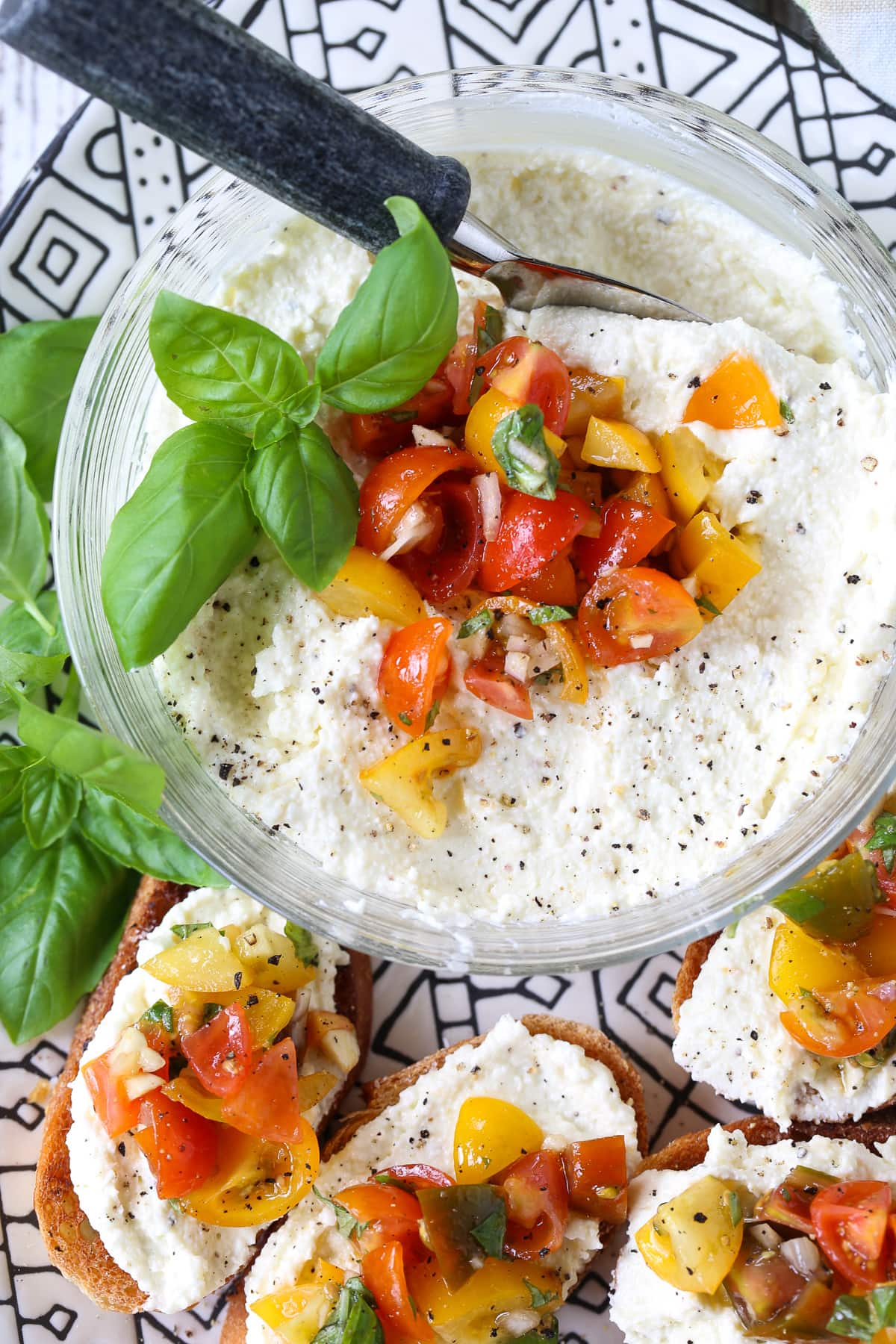 This Feta Bruschetta Recipe is a delicious, easy to make appetizer! Creamy whipped feta combined with a fresh tomato and basil topping! whipped feta in a bowl with fresh tomatoes and basil