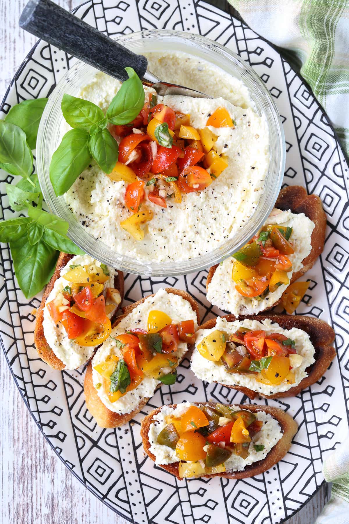 This Feta Bruschetta Recipe is a delicious, easy to make appetizer! Creamy whipped feta combined with a fresh tomato and basil topping! feta bruschetta on platter with basil