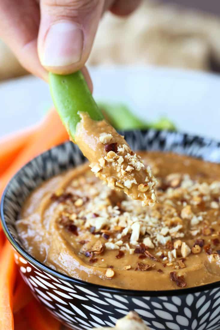 A sugar snap pea dipped in peanut sauce