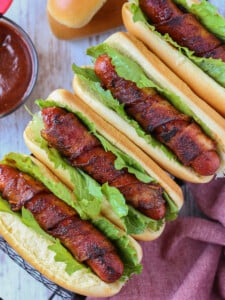 bacon wrapped hot dogs on buns with lettuce