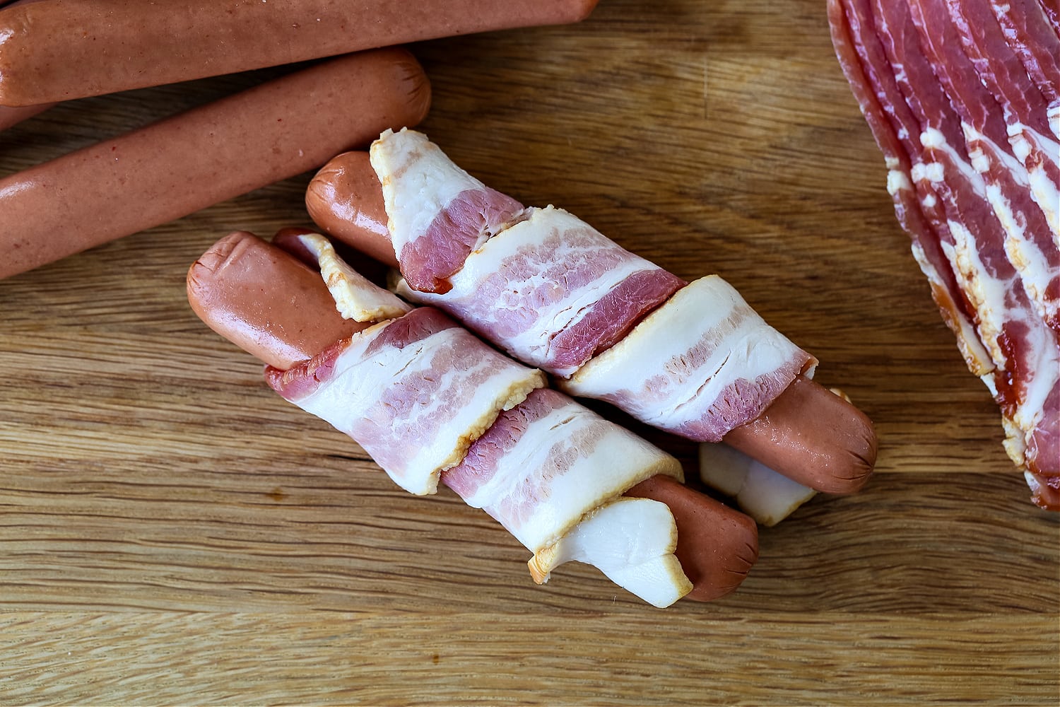 bacon wrapped around hot dogs on a board