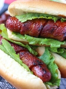 Bacon wrapped hot dogs with lettuce stacked on a plate