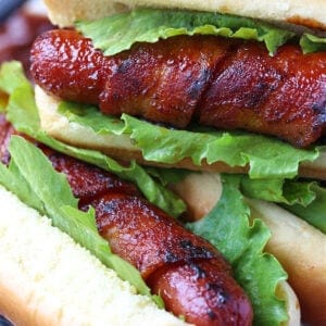 Bacon wrapped hot dogs with lettuce stacked on a plate