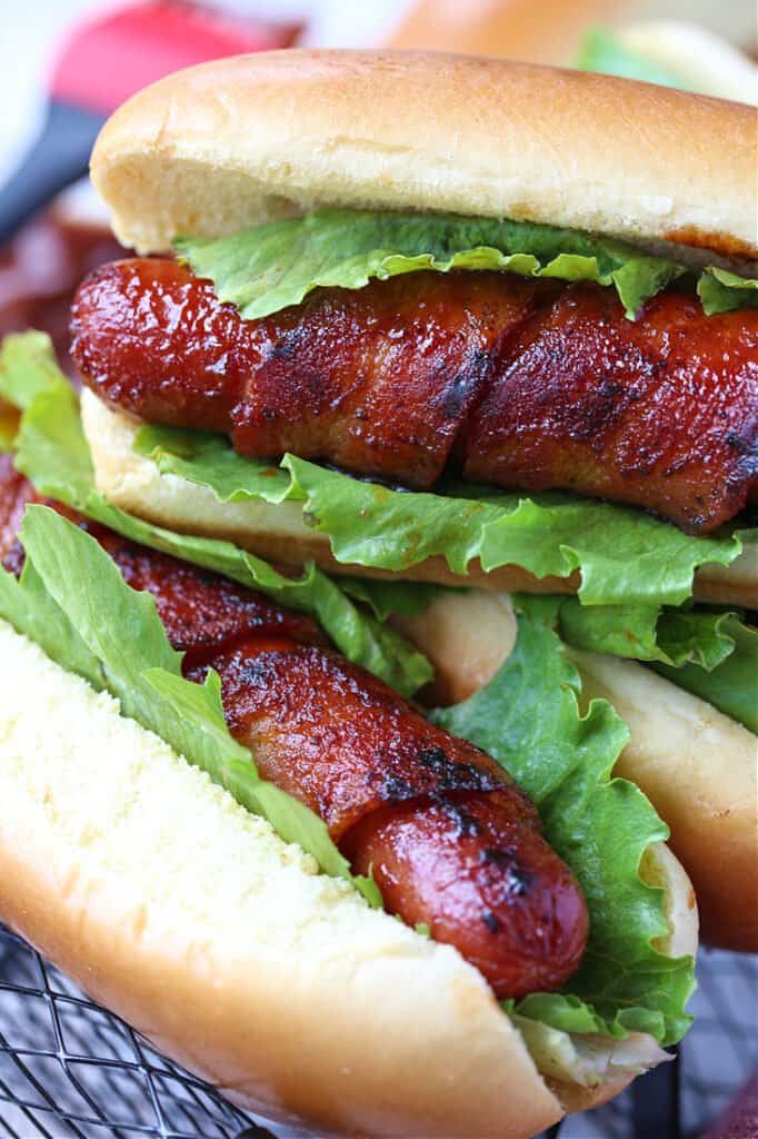 Bacon wrapped hot dogs with lettuce stacked on a plate