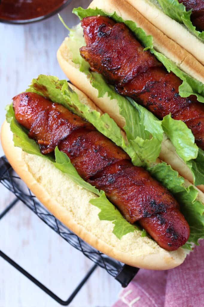 hot dog in a serving tray wrapped with bacon and served with lettuce