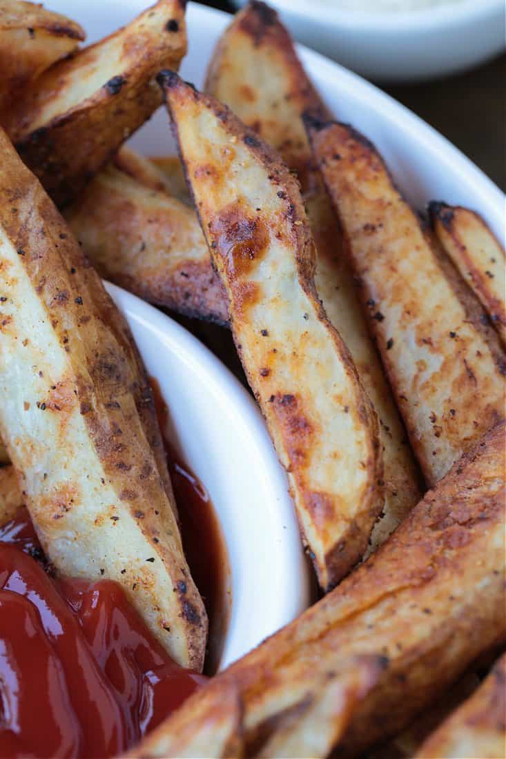 Crispy Baked Steak Fries are a delicious side dish to almost any meal! Soft, fluffy, tender insides with a crispy, perfectly seasoned crust! oven baked fries on a white bowl with ketchup