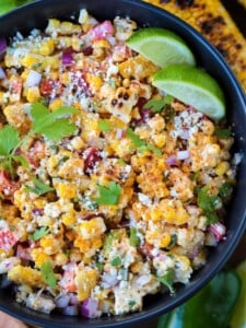 mexican street corn salad in black bowl with limes