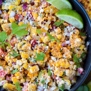 mexican street corn salad in black bowl with limes