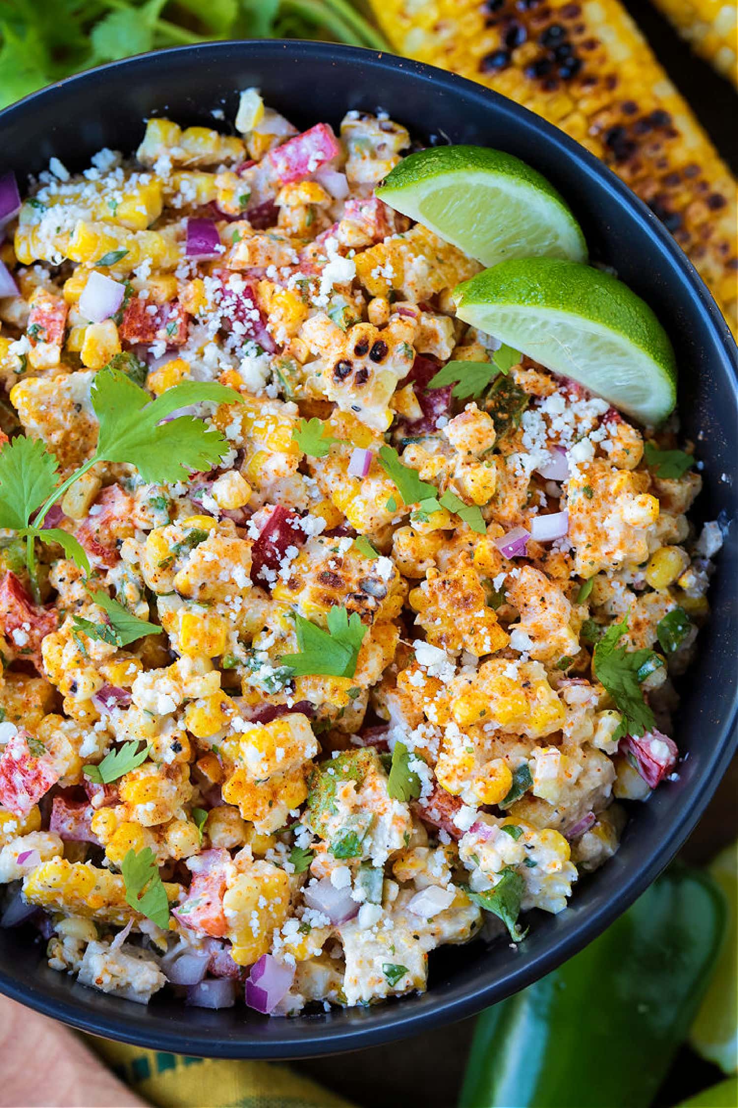 mexican street corn salad in black bowl with limes