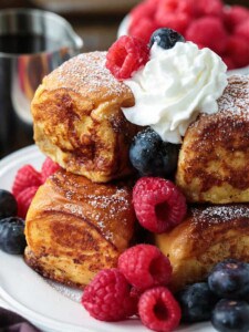 A stack of Hawaiian Roll French Toast topped with syrup, fresh berries and whipped cream.