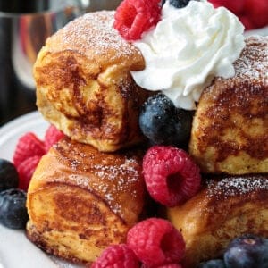 A stack of Hawaiian Roll French Toast topped with syrup, fresh berries and whipped cream.