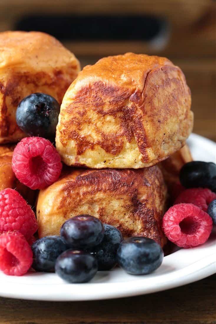 French toast rolls stacked on a plate with berries