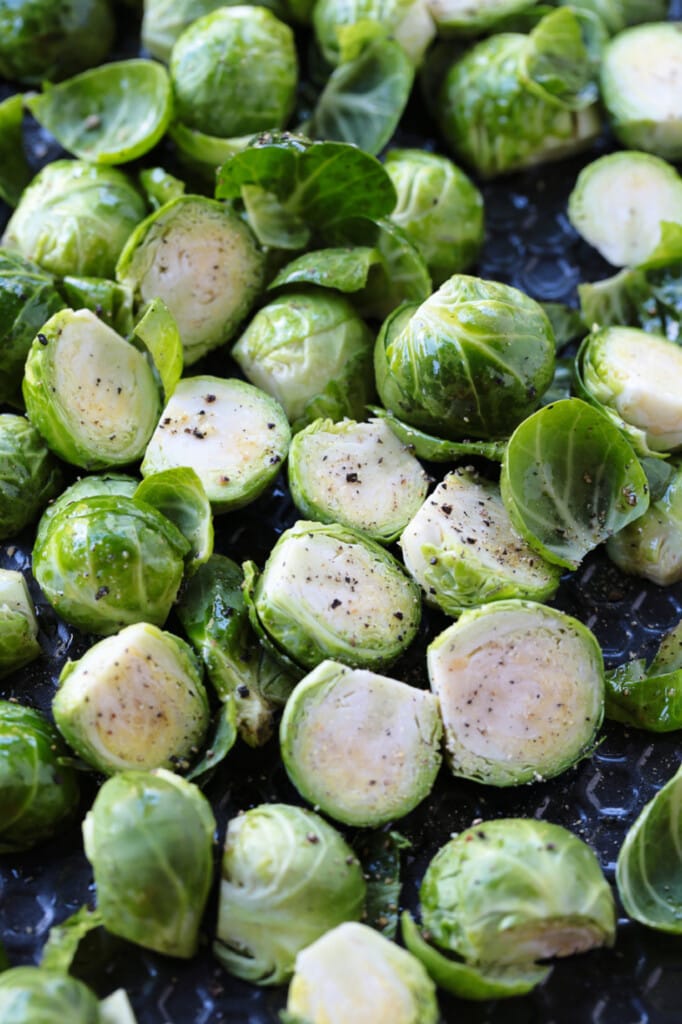 These Maple Bacon Brussels Sprouts have the perfect balance of sweet and salty! An easy to make, one pan vegetable side dish! brussels sprouts cut in half on a sheet pan with salt and pepper