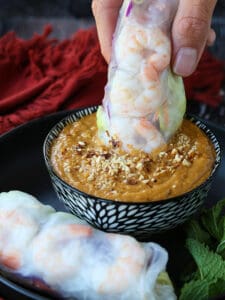 Vietnamese spring roll being sipped into peanut sauce