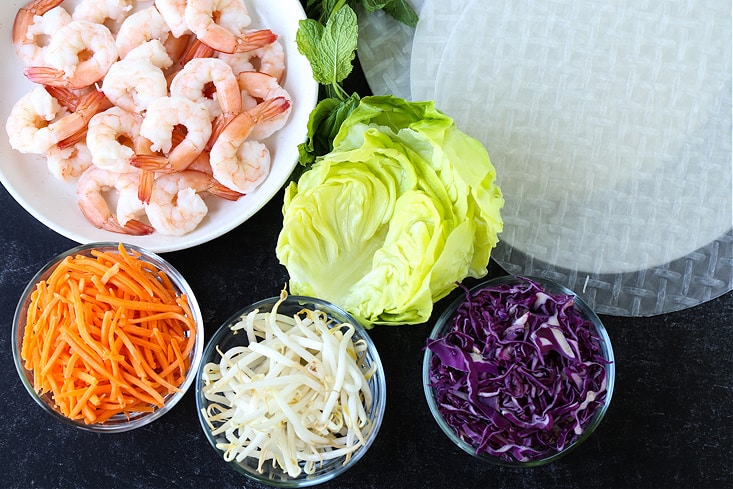 fresh vegetables and cooked shrimp next to rice paper