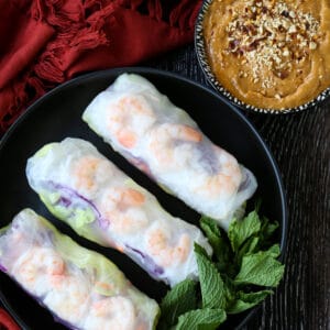 Shrimp spring rolls on a black palate with peanut sauce